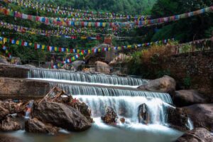 Water cascading over stepped rocks beneath rows of colourful prayer flags at Sundarijal